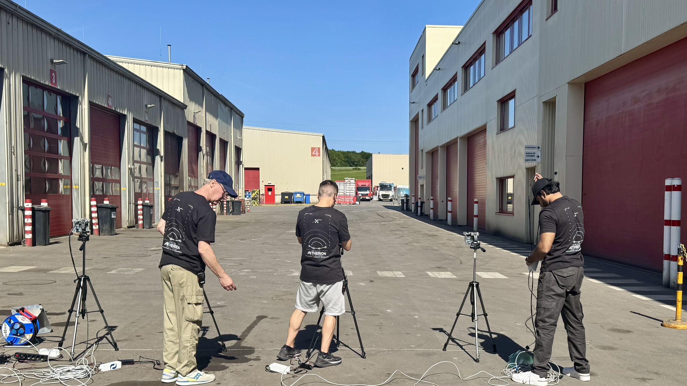 ÆTHERION Mark II.6 field validation · Lamesch site, May 2026 — three operators with tripod-mounted radar tiles and reference cameras deployed in a working logistics yard